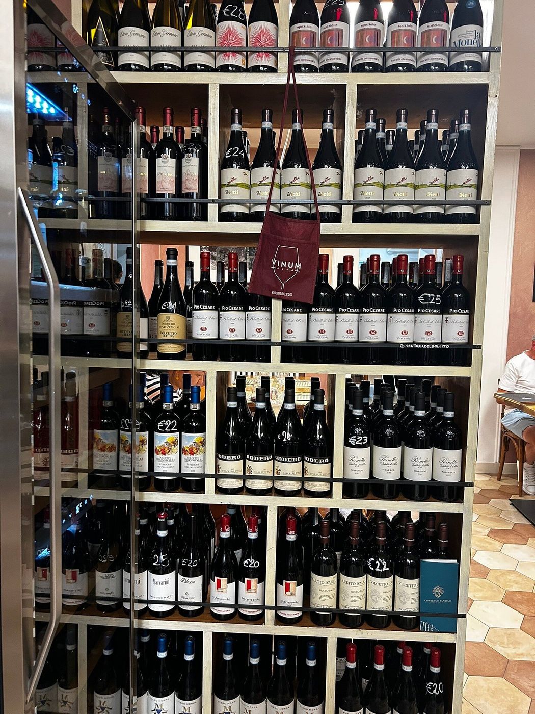 Una parete di scaffali piena di bottiglie di vini piemontesi, con i prezzi esposti