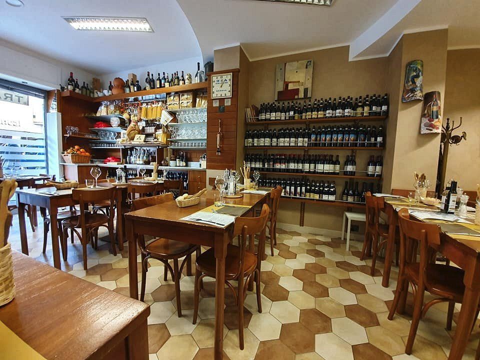 La sala con i tavoli in legno, il pavimento a esagoni e gli scaffali dei vini